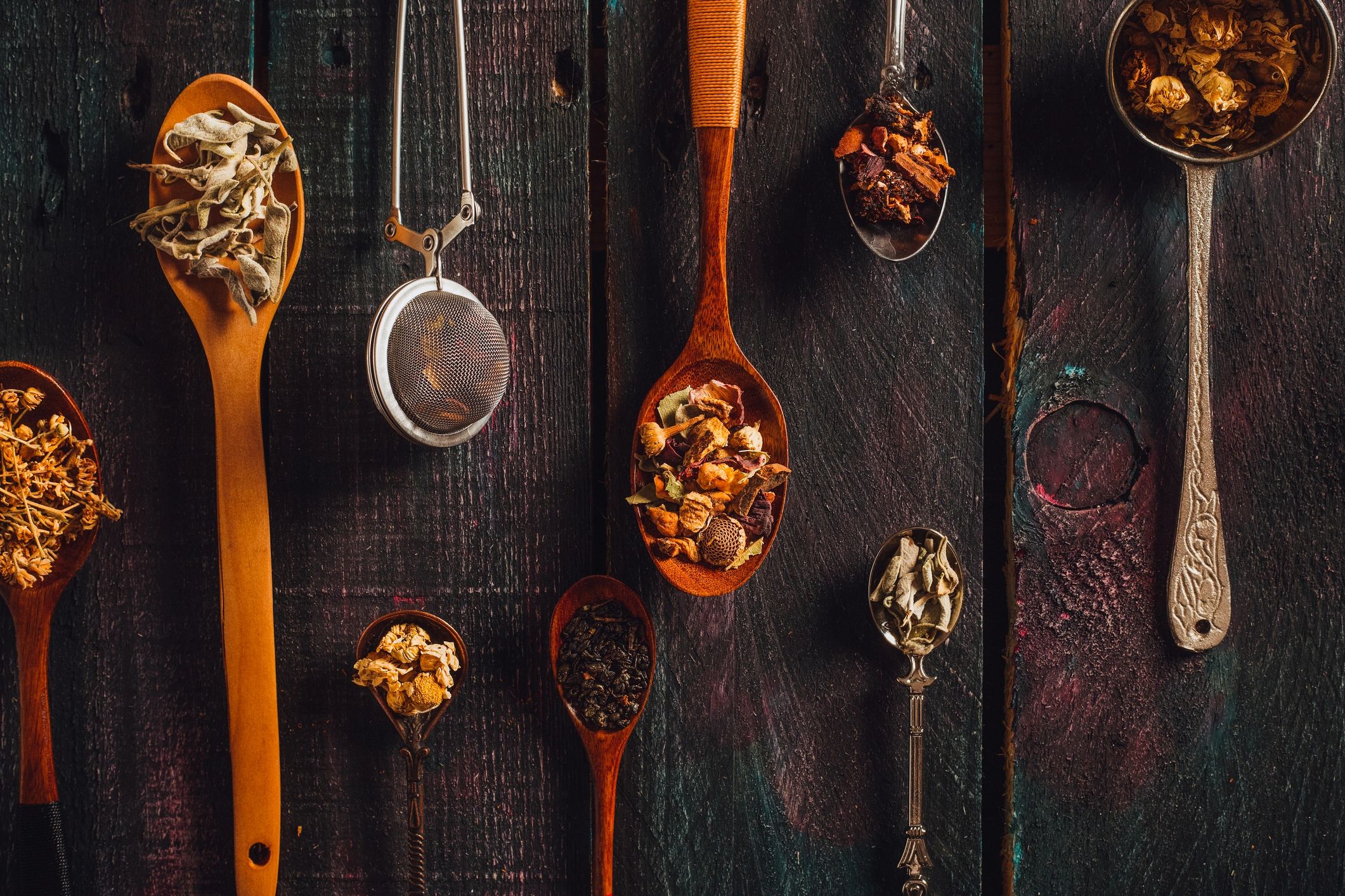 Dried herbs and leaves in spoons on a rustic wooden background